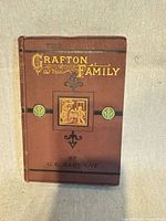 Front cover showing brown cloth boards, gilt title, black bands, green roundels, central gilt vignette