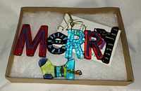 Ornament in box showing colourful fused glass letters and stocking charm