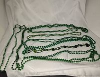Overview of all ten green bead necklaces laid out on white cloth