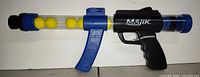 Full left-side view of Majik foam ball blaster showing four yellow balls in clear barrel