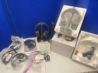 Lot overview showing wireless headphone on stand, boxed set, multiple bagged wired headphones and earphones
