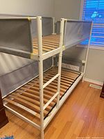 Full view of assembled white metal twin-over-twin bunk bed with wooden slats and grey guard rails