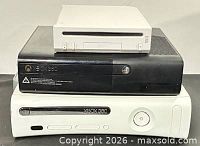 Front view of three consoles stacked: black Xbox 360 S, white Xbox 360, white Wii
