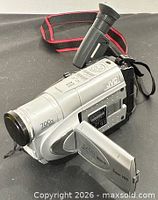 Left front view showing full camcorder, strap, lens, flip-out LCD