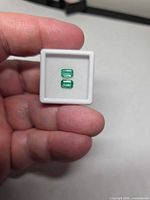 Two rectangular green emeralds in white gem box