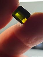 Octagon-cut forest green tourmaline held between fingers, showing color and clarity