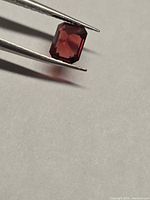 Rectangular red spinel held by tweezers, showing color and facets