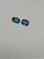 Two oval deep blue zircon gemstones on neutral background