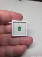 Emerald gemstone in display case held between fingers
