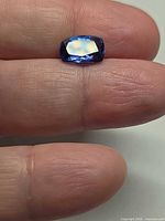 Cushion-cut tanzanite on fingertip showing size and color