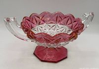 Side view of pressed glass candy dish showing pink scalloped rim, clear starburst body, octagonal pink foot, dual handles