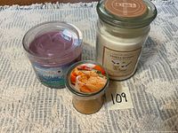 Three unused jar candles: Vanilla Nutmeg, purple scented, Trueliving Orange Cream