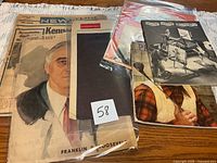 Stacked newspapers and magazines in plastic sleeves, visible FDR cover and booklet