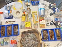 Overview of entire lot on round table showing nails, screws, organizer trays, plumbing and electrical components, rope, duct, adhesive