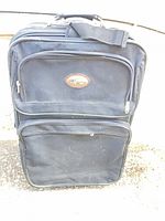 Front view of black rolling suitcase showing two zippered exterior pockets and logo plate