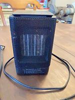Front view of black portable space heater showing mesh grille and power cord