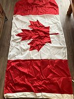 Full view of Canadian flag lying flat showing maple leaf design, pole sleeve hem and wrinkles
