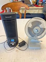Honeywell tower fan-heater and gray desk fan with cords on tabletop