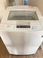 Front perspective of LG top-load washer showing overall exterior and brand badge