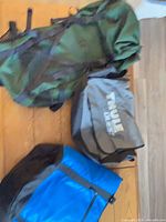 All three backpacks on table: green, gray Thule, blue cooler style