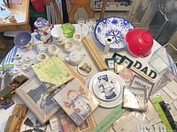 Overall view of assorted ceramics, glassware, signs, picture frames, toy car and paper goods on table