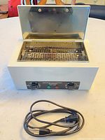 Sterilizer open showing stainless tray, glass lid, exterior housing, and power cord