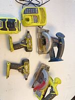 All six Ryobi tools laid out: charger, speaker, two impact drivers, two circular saws