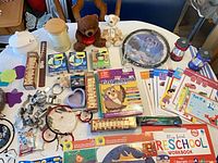 Overall lot layout showing tin, plush bears, cookie cutters, dreamcatchers, LED lights, workbooks, Pokémon pack, ruler, plates