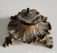 three-quarter view of ornate cast metal inkwell showing lid, scalloped base and leaf feet