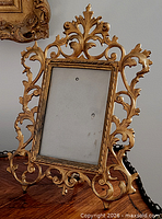 Front view of ornate gilt metal frame showing scrollwork and glass