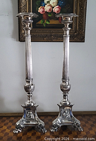 Full view of both tall silver-plated candlesticks standing side by side