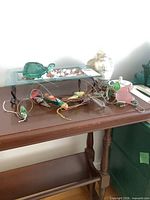Lot overview showing glass tray with turtle, angel figurine, parrot mobile components on table