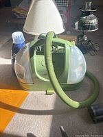 Bissell Little Green cleaner with hose, cleaning solution bottle, lamps in background