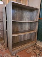 Front angled view of both matching laminate bookshelves showing three shelves and wood-grain finish