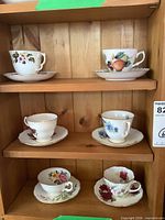 Six bone china cup and saucer sets on cabinet shelves