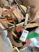 Bin containing leather tool belt, red clamp, claw hammer, horseshoe and other tools