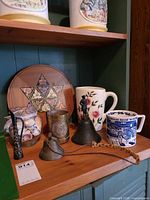 All items together on shelf: mugs, pitcher, trivet, seashells, bells