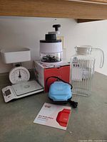 Group view showing waffle maker, spiralizer on box, analog scale, digital scale, glass pitcher