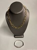 Gold-tone chainlink necklace on display stand with bangle below