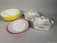 Group shot showing two Corning Ware casseroles with lids, Pyrex yellow mixing bowl, pink-rimmed pie plate
