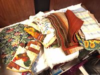 Assorted patterned placemats, oven mitt and pot holders on surface