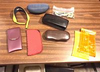 Overview showing strap, blue case, bagged cloth, black case, purple case, red pouch, brown case, orange and yellow sleeves