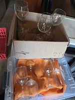 Cardboard box containing several clear glass red wine glasses, showing quantity and condition