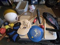 Overview of lot on table showing helmets, rackets, cap, flying disc, balls, pads