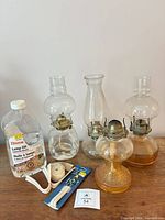 Group shot of four oil lamps, lamp oil bottle, wick roll and packaged wicks