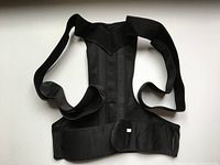Front view of black posture support brace showing mesh panel and Velcro waist strap
