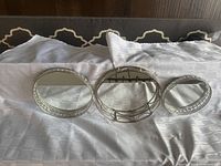 Three round silver-tone mirrored trays displayed side by side on cloth backdrop