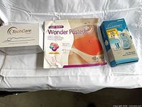 Front view of all three boxed items: TechCare massager, Lazy Body patch, Omron ElectroTherapy device