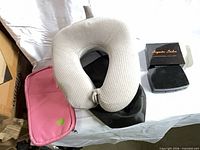 Neck pillow, black bag beneath, pink zippered pouch to left, boxed eyelash kit and compact case to right