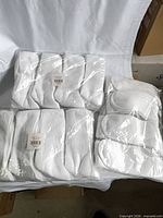 Three sealed plastic packs of white ribbed crew socks on table